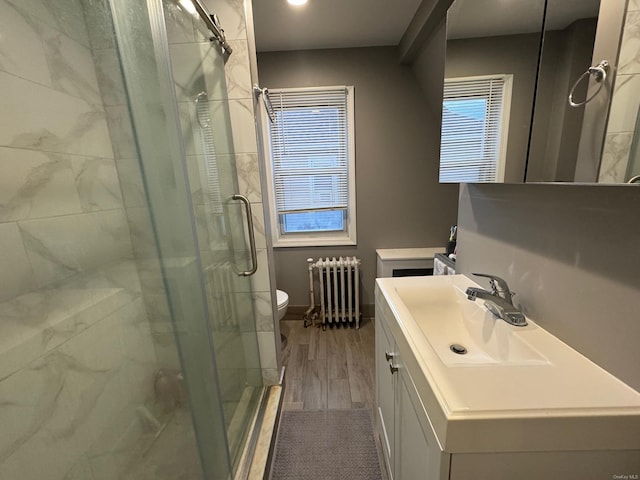 bathroom with hardwood / wood-style floors, vanity, radiator heating unit, toilet, and a shower with shower door