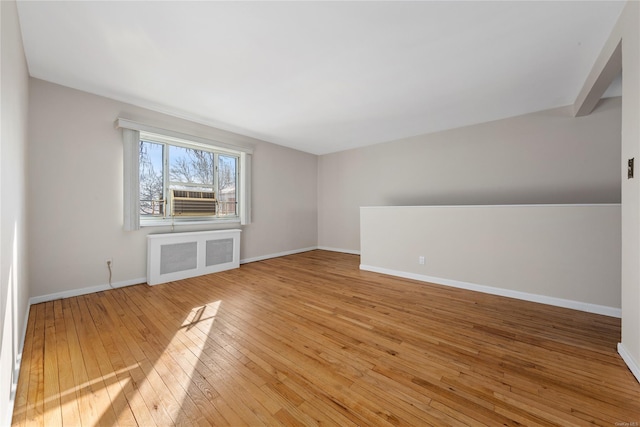 unfurnished living room with cooling unit, radiator, beamed ceiling, and light wood-type flooring