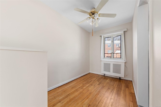 spare room featuring ceiling fan, radiator heating unit, and light wood-type flooring