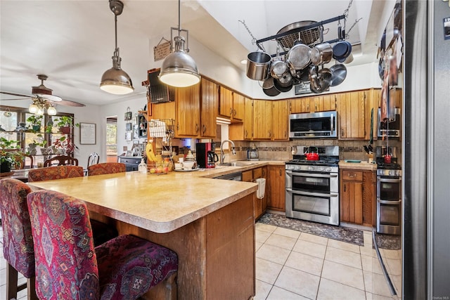 kitchen with pendant lighting, decorative backsplash, light tile patterned floors, appliances with stainless steel finishes, and kitchen peninsula