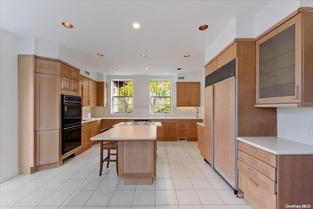 kitchen with a center island, paneled fridge, black double oven, a breakfast bar, and light tile patterned floors