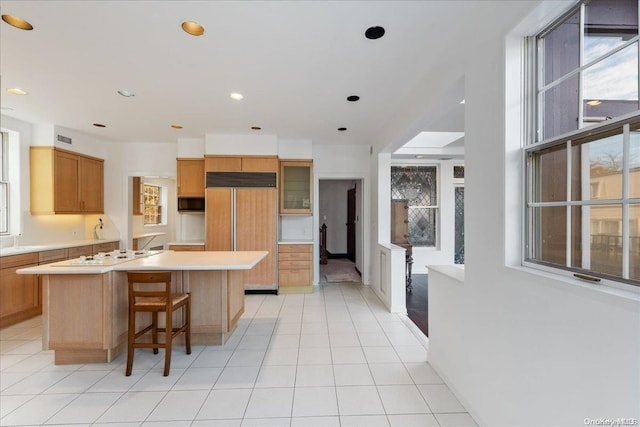 kitchen with light tile patterned flooring, a kitchen bar, a kitchen island with sink, and paneled built in fridge