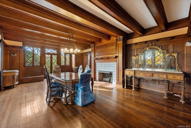 dining room with wood-type flooring, a brick fireplace, wooden walls, and beam ceiling