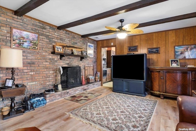 living area featuring wooden walls, beamed ceiling, light wood finished floors, a fireplace, and ceiling fan
