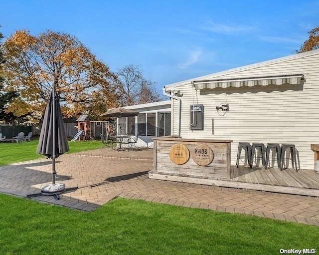 back of house featuring a sunroom, a yard, a deck, a playground, and a patio area