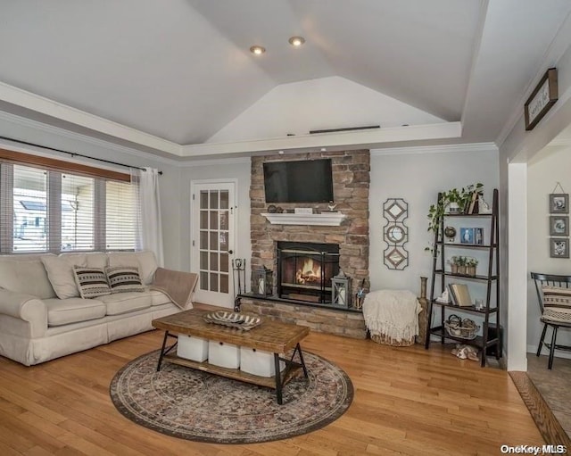 living room featuring a raised ceiling, crown molding, a fireplace, and light wood-type flooring