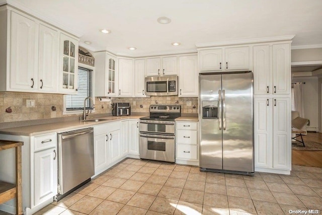 kitchen with appliances with stainless steel finishes, ornamental molding, sink, light tile patterned floors, and white cabinetry