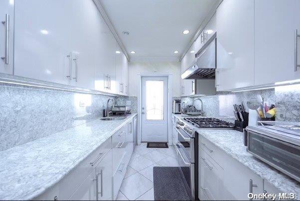 kitchen with high end range, tasteful backsplash, sink, white cabinetry, and range hood