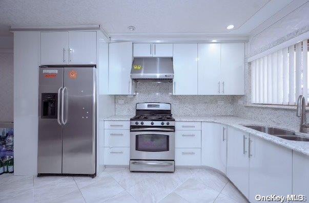 kitchen featuring appliances with stainless steel finishes, light stone counters, wall chimney exhaust hood, sink, and white cabinets