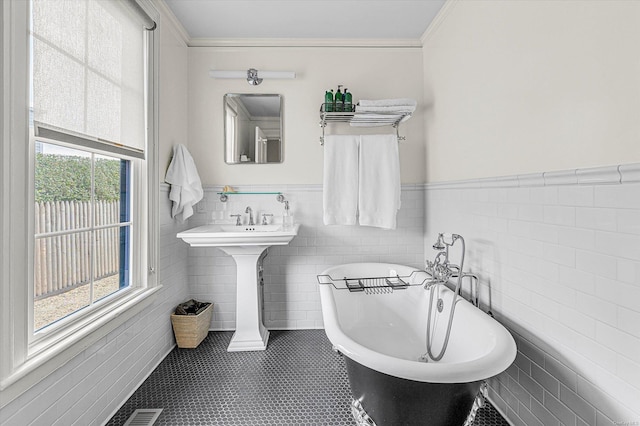 bathroom with a wealth of natural light, a bathtub, tile walls, and ornamental molding