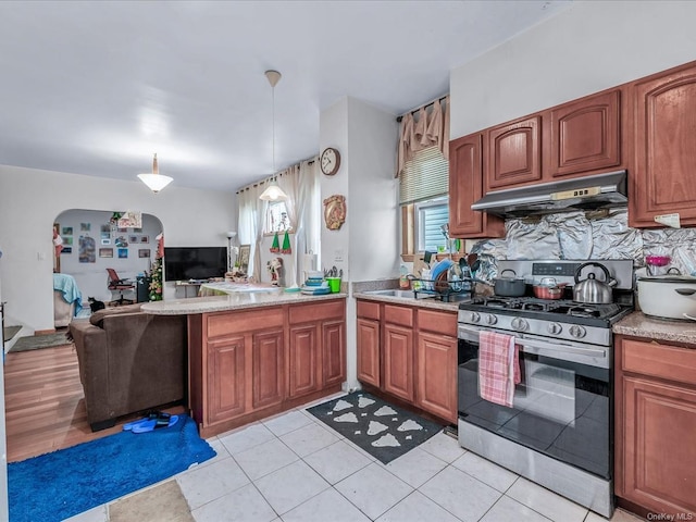 kitchen featuring decorative backsplash, exhaust hood, stainless steel range with gas stovetop, hanging light fixtures, and light tile patterned flooring