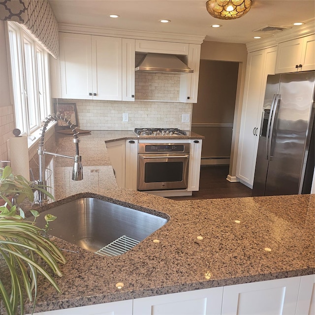 kitchen featuring wall chimney exhaust hood, white cabinetry, appliances with stainless steel finishes, and dark stone counters