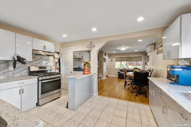 kitchen featuring backsplash, an AC wall unit, white cabinets, stainless steel range with gas cooktop, and light tile patterned flooring