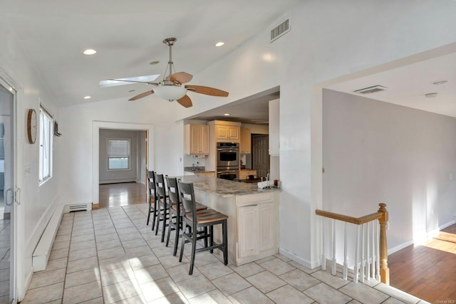 kitchen with vaulted ceiling, ceiling fan, light tile patterned floors, light stone counters, and a kitchen bar