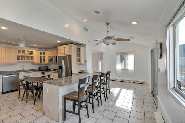 kitchen featuring lofted ceiling, a kitchen breakfast bar, baseboard heating, stone countertops, and stainless steel appliances