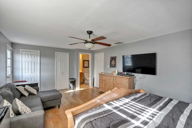 bedroom with ceiling fan, two closets, connected bathroom, and light hardwood / wood-style flooring