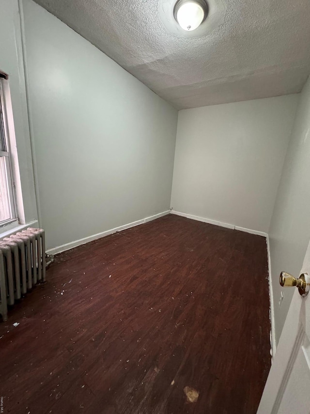 spare room featuring a textured ceiling, radiator, and dark wood-type flooring