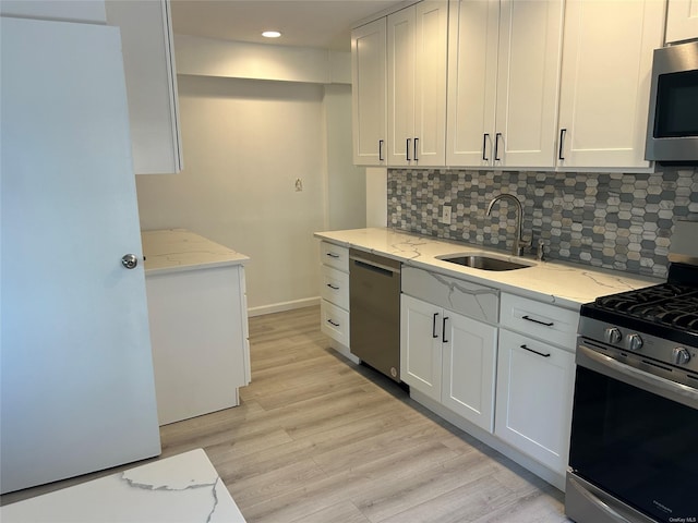 kitchen with appliances with stainless steel finishes, light stone counters, white cabinetry, and sink