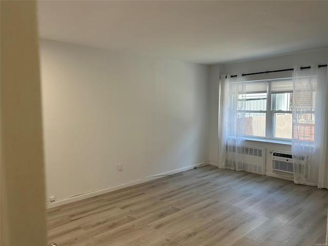 unfurnished room featuring cooling unit, light wood-type flooring, and radiator heating unit