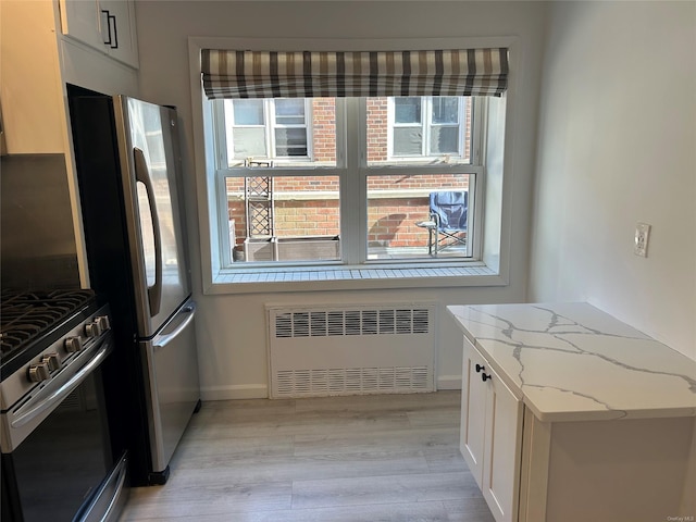 kitchen with radiator, white cabinets, light hardwood / wood-style floors, light stone counters, and stainless steel appliances