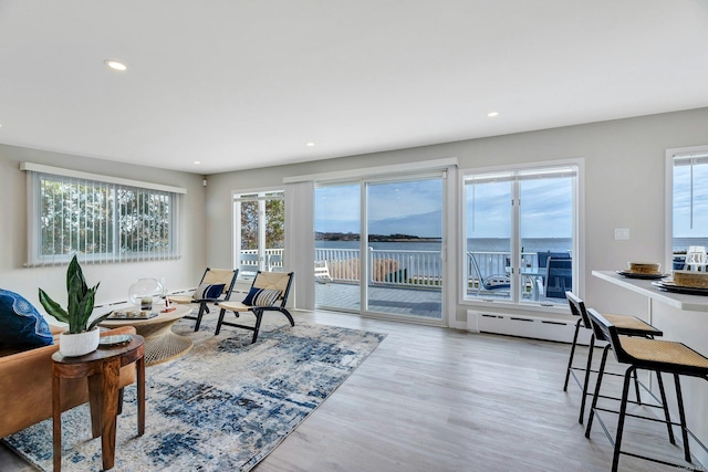 living room with a baseboard heating unit, a water view, and light hardwood / wood-style floors