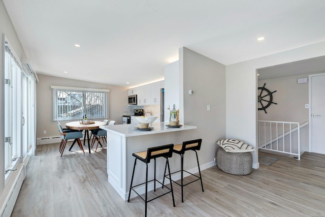 kitchen featuring a kitchen breakfast bar, tasteful backsplash, light hardwood / wood-style flooring, kitchen peninsula, and white cabinets