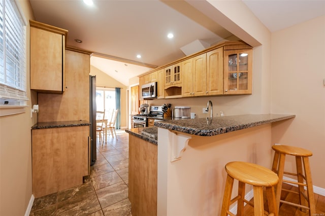 kitchen with kitchen peninsula, stainless steel appliances, light brown cabinets, a breakfast bar area, and lofted ceiling