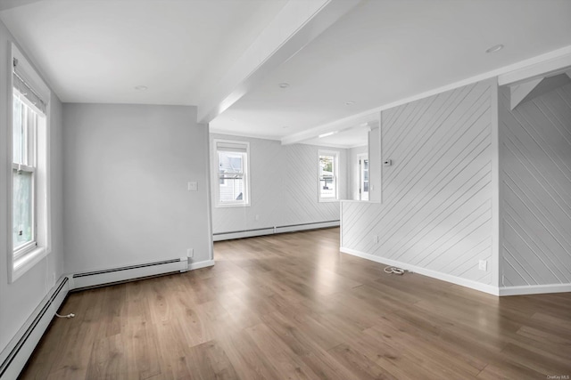 unfurnished room with a baseboard heating unit, wood walls, and a healthy amount of sunlight