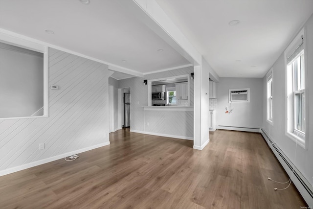 unfurnished living room featuring an AC wall unit, a baseboard radiator, hardwood / wood-style flooring, and a healthy amount of sunlight