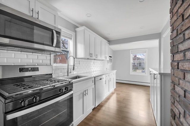 kitchen with baseboard heating, appliances with stainless steel finishes, white cabinetry, and sink