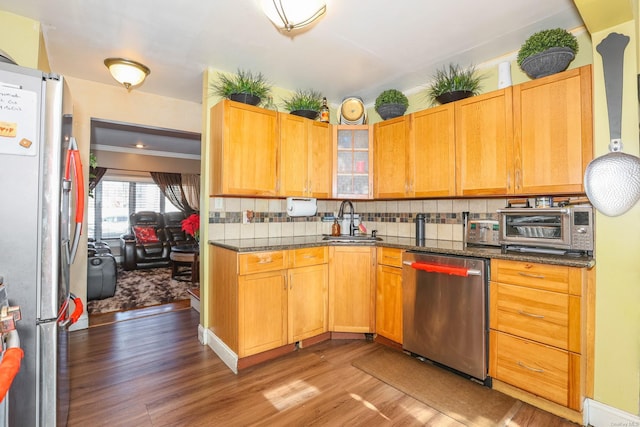 kitchen featuring tasteful backsplash, stainless steel appliances, sink, wood-type flooring, and dark stone countertops