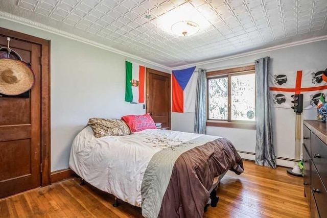 bedroom with hardwood / wood-style floors, baseboard heating, and crown molding