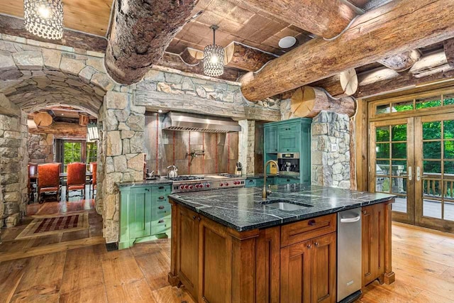 kitchen with french doors, wall chimney exhaust hood, sink, an island with sink, and light wood-type flooring