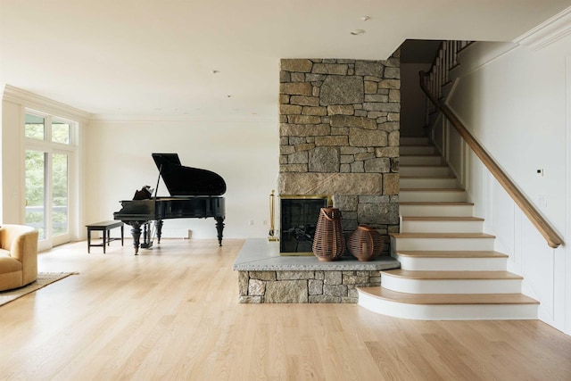 stairway with a stone fireplace, wood-type flooring, and ornamental molding