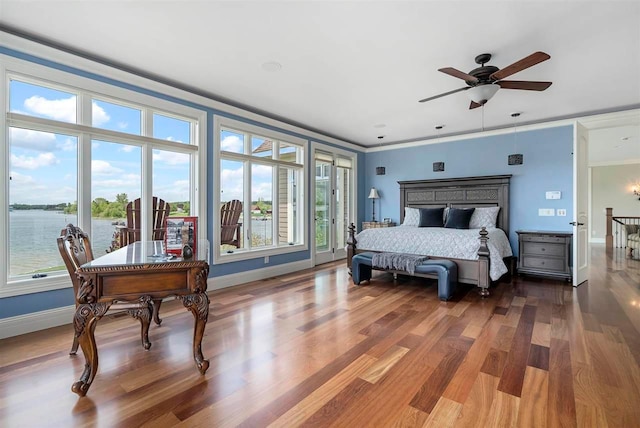 bedroom with dark hardwood / wood-style floors, a water view, ceiling fan, and multiple windows