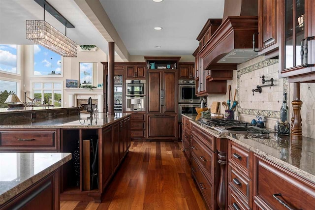 kitchen featuring dark hardwood / wood-style floors, stainless steel appliances, dark stone counters, tasteful backsplash, and pendant lighting