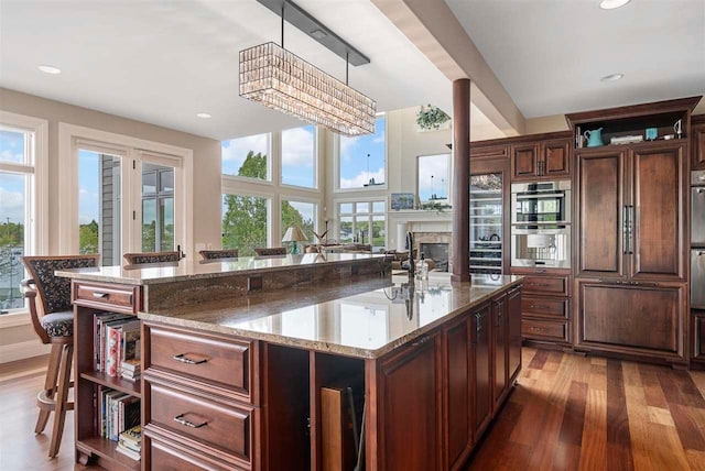 kitchen featuring pendant lighting, a center island, hardwood / wood-style floors, stainless steel double oven, and light stone counters