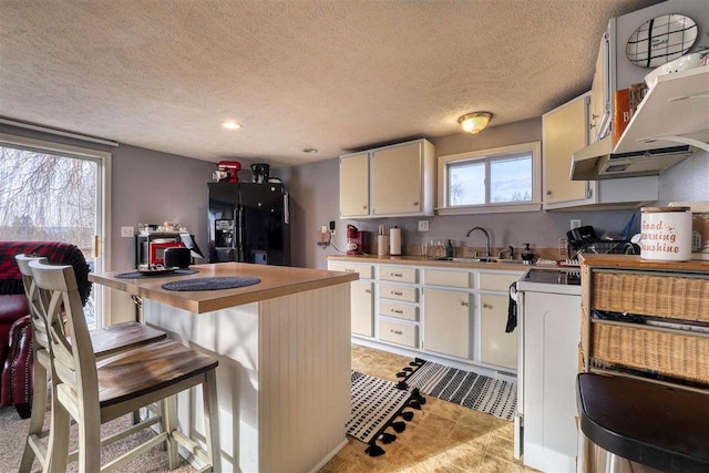 kitchen with sink, black fridge, a textured ceiling, a breakfast bar area, and white cabinets