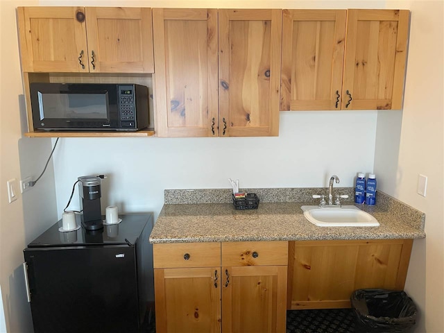 kitchen featuring light stone countertops, sink, and refrigerator