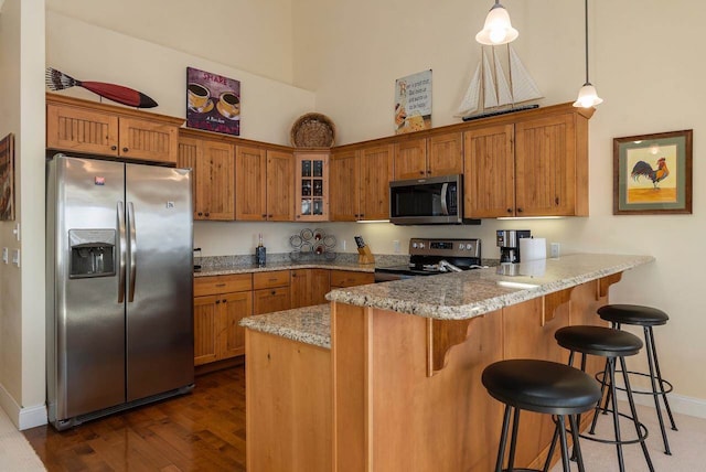 kitchen with pendant lighting, stainless steel appliances, a kitchen bar, light stone countertops, and dark wood-type flooring