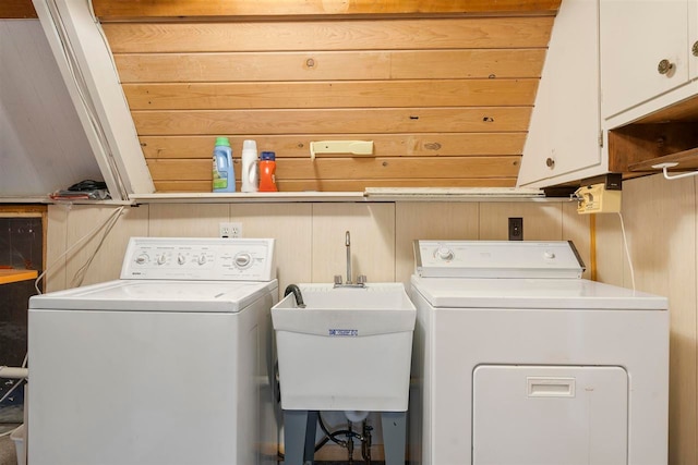 washroom featuring cabinets, wood walls, washing machine and clothes dryer, and sink