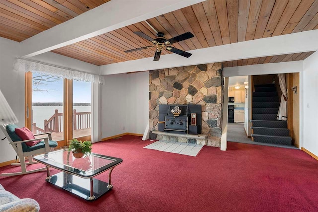 living room with a water view, a wood stove, wooden ceiling, carpet flooring, and ceiling fan