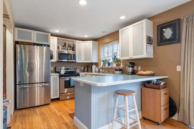 kitchen with kitchen peninsula, stainless steel appliances, white cabinets, and light wood-type flooring