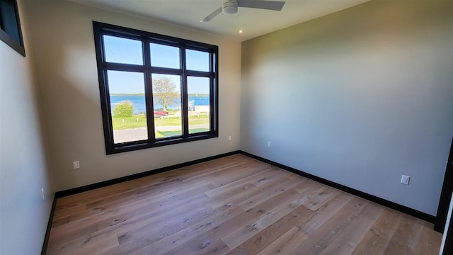 unfurnished room featuring a water view, light wood-type flooring, and ceiling fan