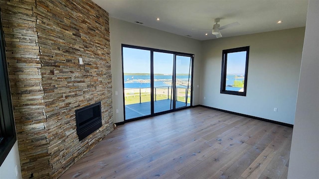 unfurnished living room featuring a fireplace, a water view, ceiling fan, and wood-type flooring