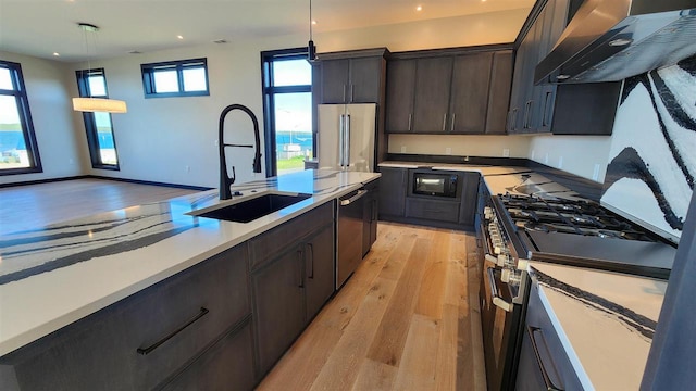 kitchen with wall chimney range hood, pendant lighting, dark brown cabinetry, light hardwood / wood-style floors, and high quality appliances