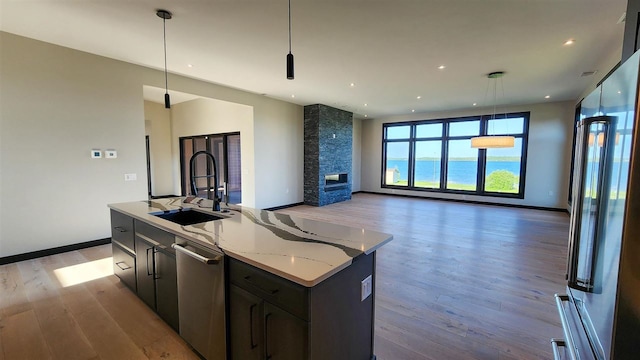 kitchen featuring pendant lighting, an island with sink, light wood-type flooring, sink, and a stone fireplace