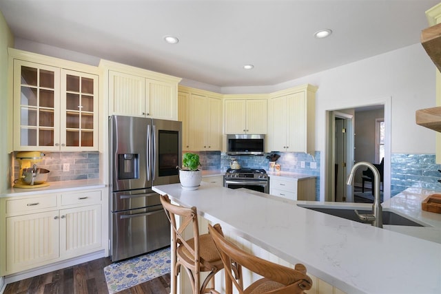 kitchen featuring light stone countertops, dark wood-type flooring, appliances with stainless steel finishes, a breakfast bar, and tasteful backsplash