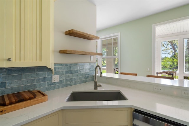 kitchen with tasteful backsplash, dishwasher, light stone counters, sink, and cream cabinetry