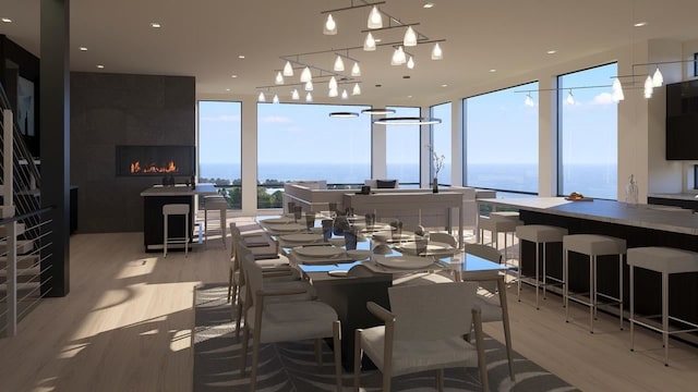 dining room featuring floor to ceiling windows, a fireplace, a water view, and light hardwood / wood-style flooring